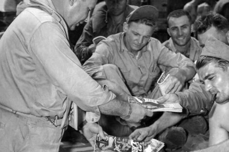 Lt. John Slivka, a Special Service officer, passes out pulp magazines to GIs aboard the USS Tyler heading to Baker Island. The GIs were en route to the Pacific island to establish a staging base for bombers.
