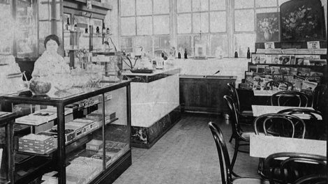 A woman stands at the counter of a drug store sometime in the first half of 1925. Along the bottom row of the magazine rack on the right are copies of the pulp magazines "Flynn's," "Blue Book," "Action Stories," "Love Story," "Breezy Stories," "Detective Fiction Weekly," "Snappy Stories" and "Argosy All-Story Weekly."