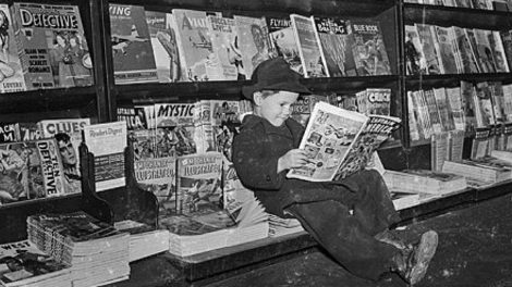 A kid reads a comic book at this newsstand in March 1942, while a few pulps are on display behind him.